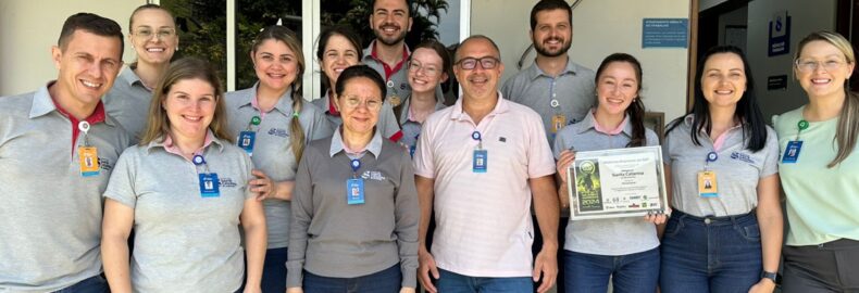 Equipe multidisciplinar do SESMT do HSC Blumenau segurando certificado de melhor empresa de Segurança e Saúde no Trabalho, na categoria Hospitalar